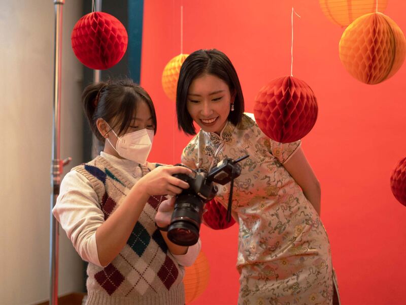 Aileen showing the back of her camera to a model on a red set hung with paper lanterns