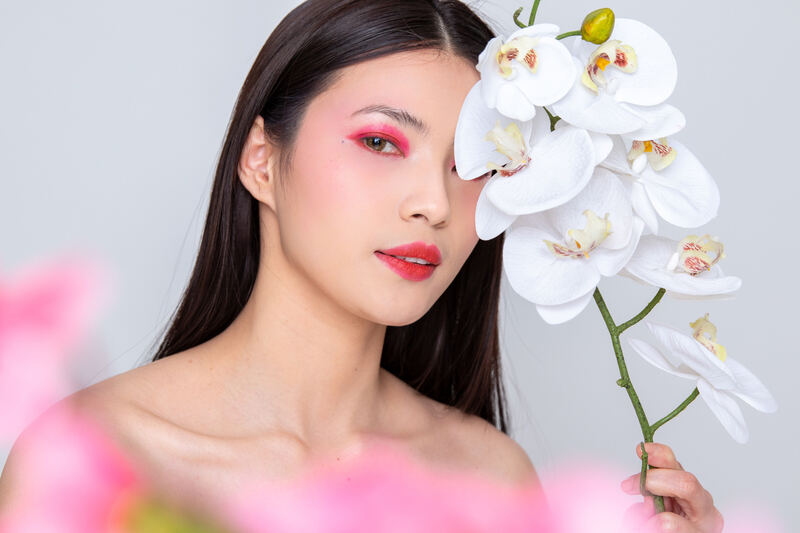 Beauty portrait of a woman with pink eyeshadow holding a white orchid stem