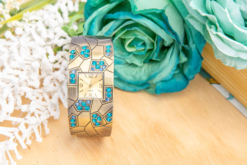 A turquoise mosaic cuff watch on a wood surface beside teal roses