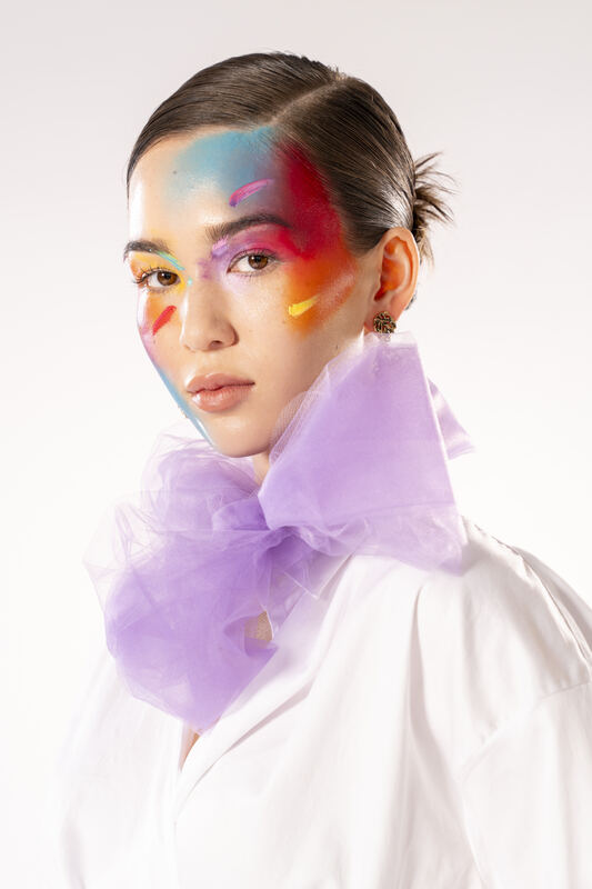 Portrait of a model with bold rainbow face paint and a lilac organza collar