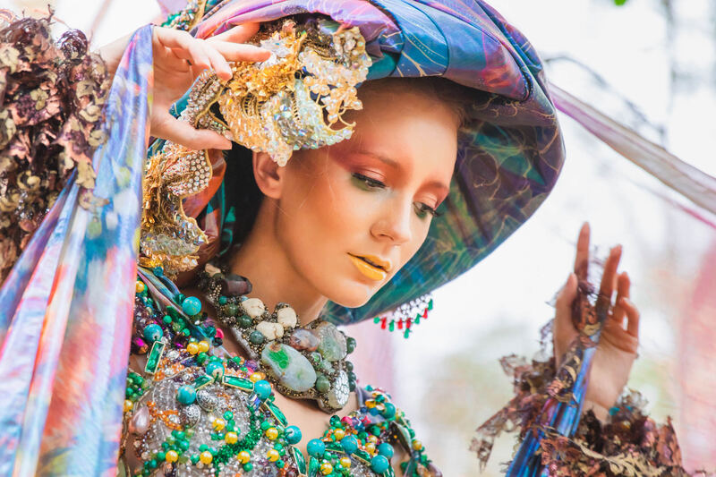 Model in a jewelled headwrap and colourful beaded collar among dried florals