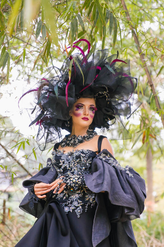 Model in a sculptural black feathered headpiece and ruffled gown in a bamboo grove