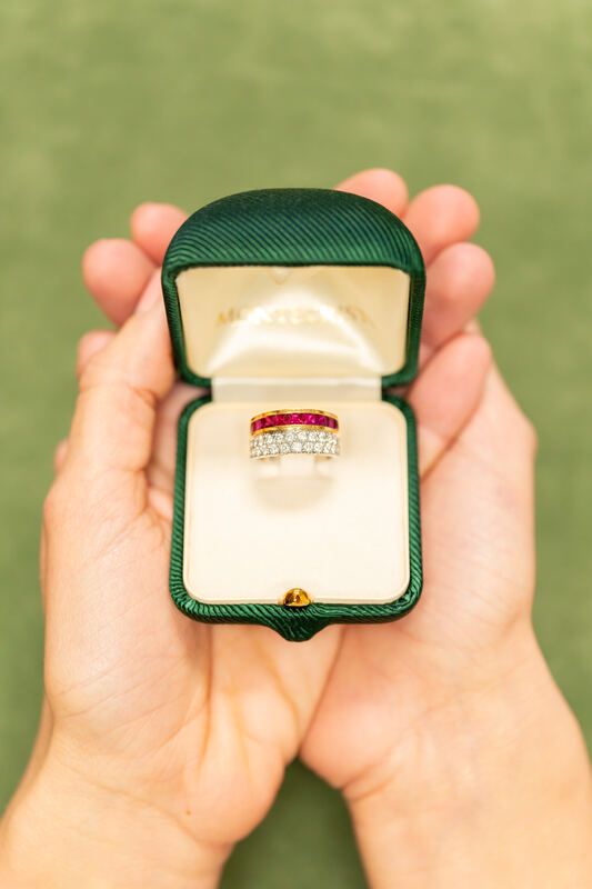 Hands holding an open green ring box with a ruby and diamond ring