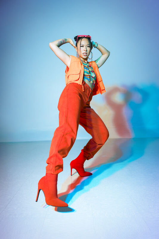 A dancer in an orange outfit and boots striking a pose against a blue backdrop