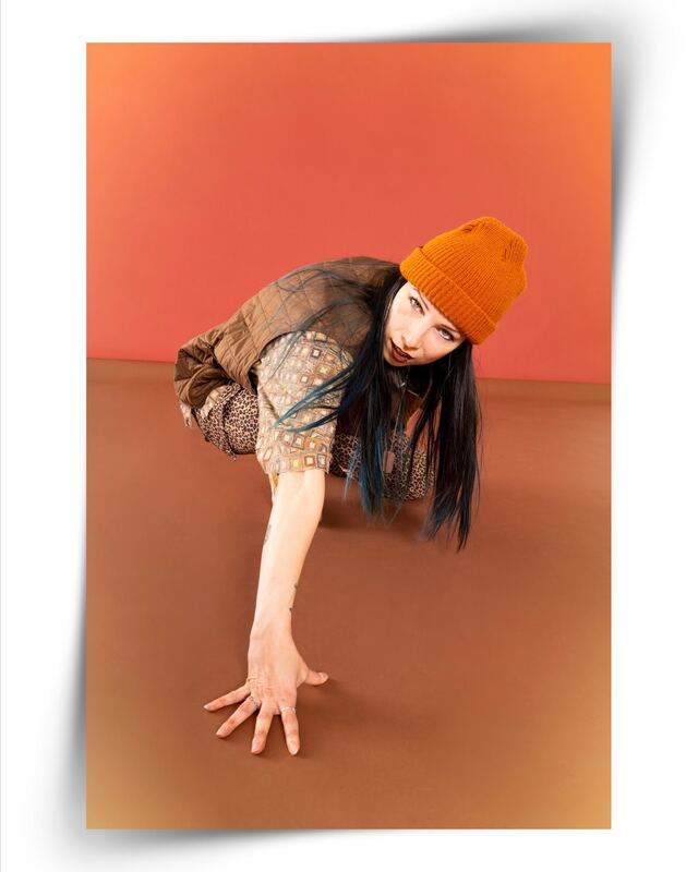 A Diamonds Crew dancer in a camo jacket and orange beanie low to the floor on a terracotta backdrop