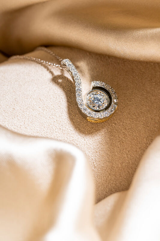 A swirl diamond pendant resting on satin fabric