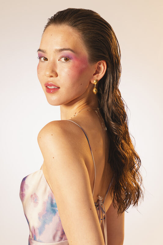 Profile portrait of a woman with a long braid and pink eyeshadow on a peach backdrop