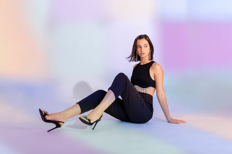 A model in black seated on the floor against pastel blurred light