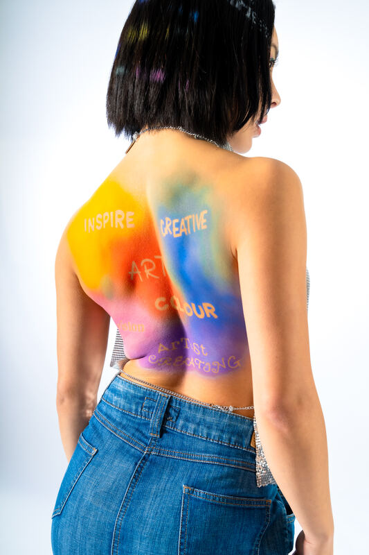 A woman's bare back painted with rainbow brushstrokes and words, wearing jeans