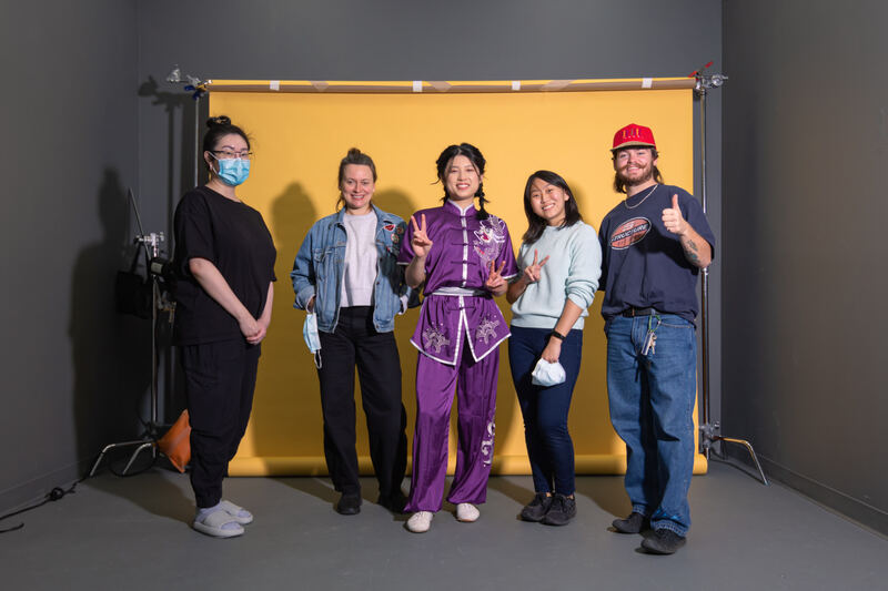 A wushu performer in purple with a team of crew on a yellow studio set