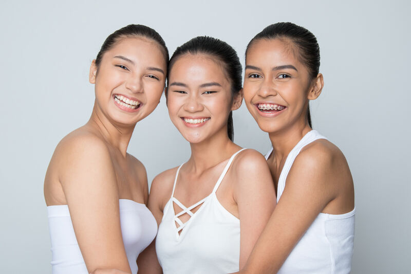 Three smiling women in white tops posed close together on light grey